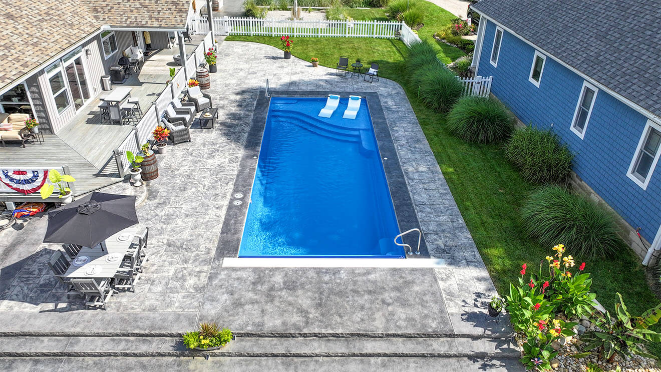Installed Aspen fiberglass pool with stamped concrete deck and ledge loungers