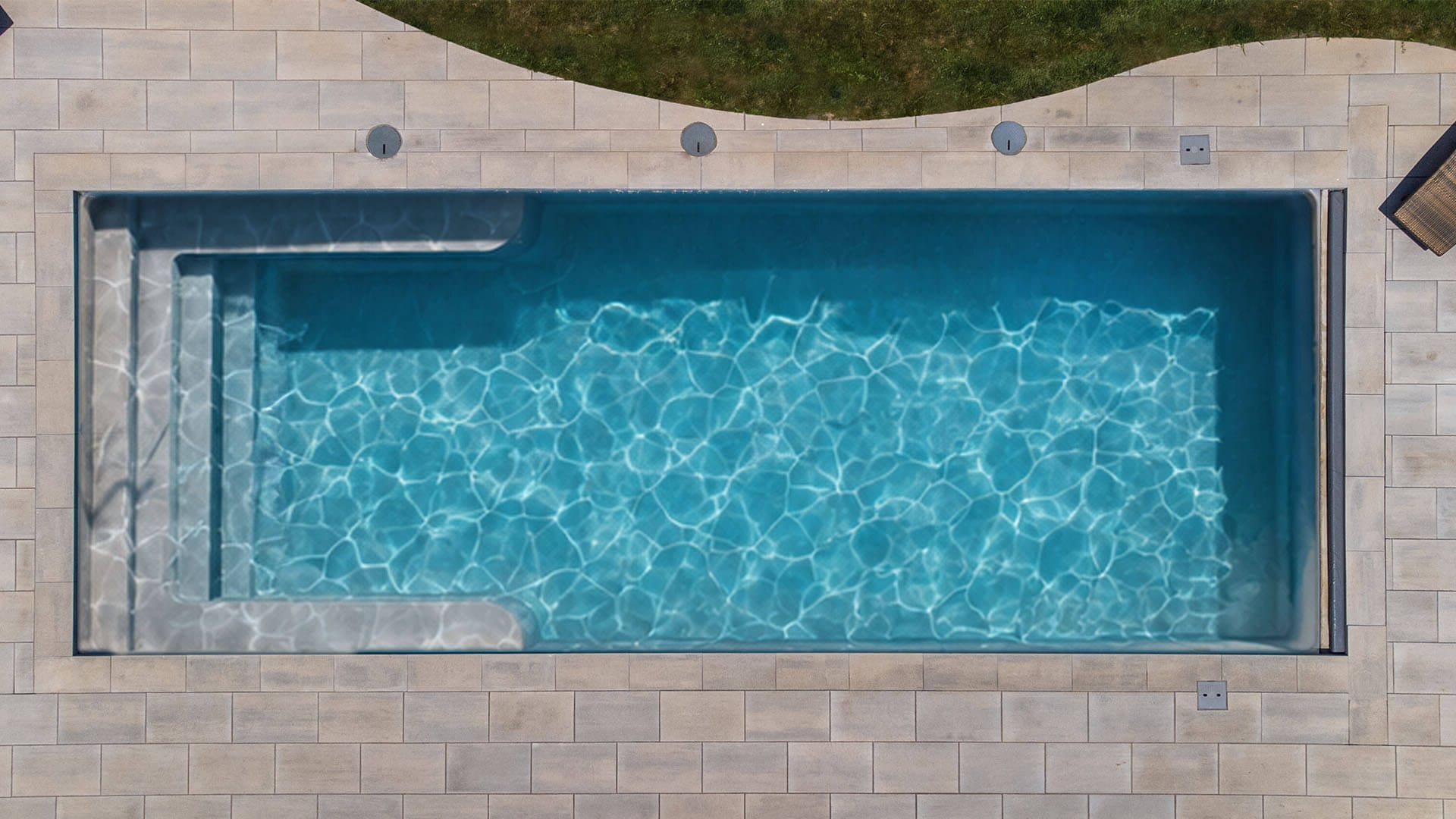 Installed Big Bob fiberglass pool with wraparound bench and paver deck, seen from above