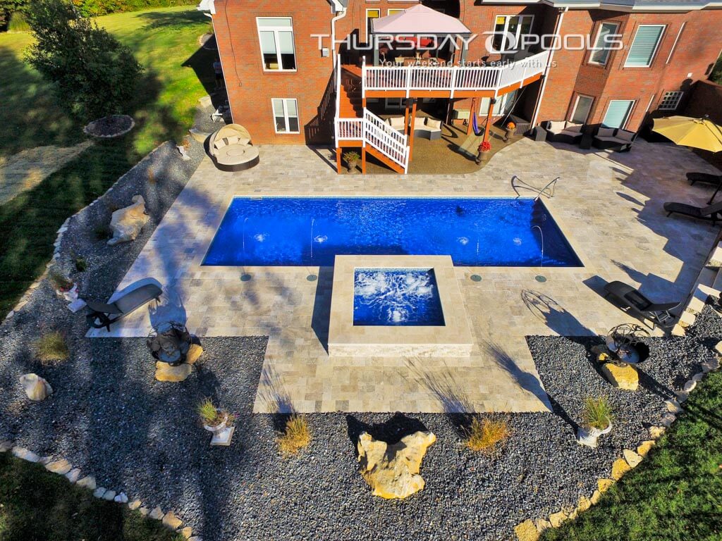 Installed Goliath fiberglass pool with spillover spa and travertine deck