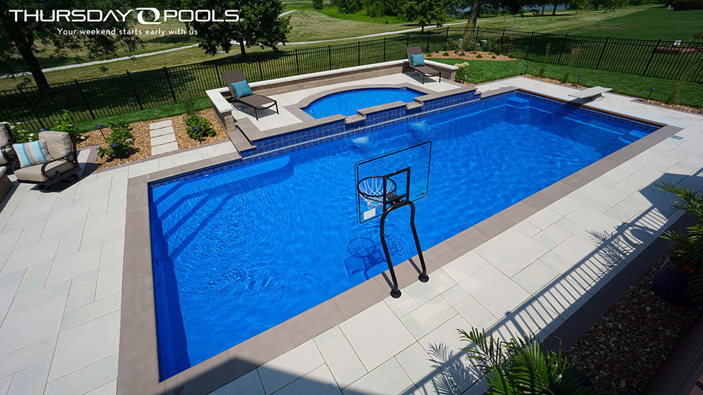 Installed Monolith fiberglass pool with raised spillover spa and paver deck