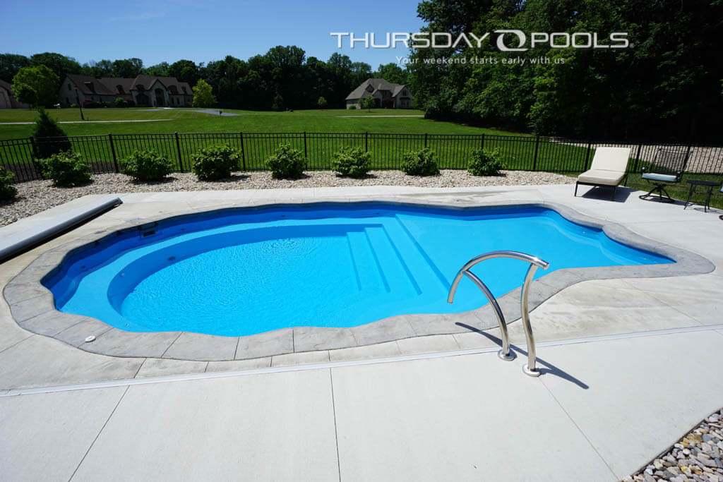 Installed Pearl fiberglass pool with scalloped edges and stamped concrete deck