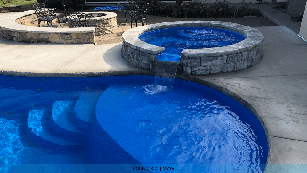 Installed round fiberglass spa with stone wall spilling over into the pool
