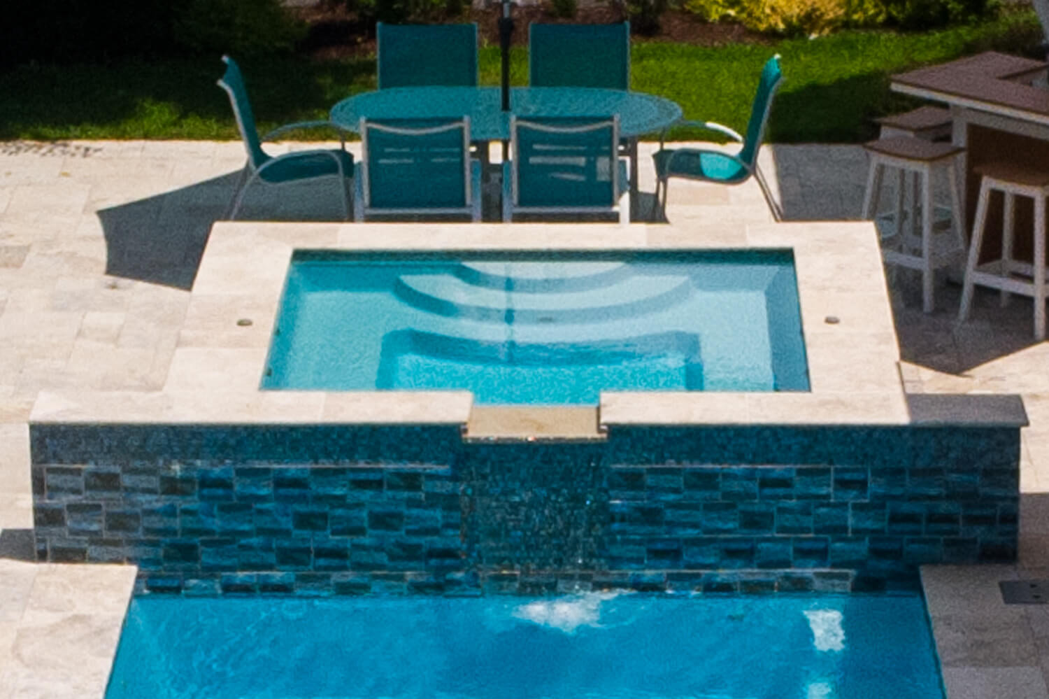 Installed square fiberglass spa with tiled spillover wall and travertine coping